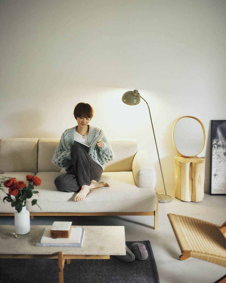 フロアランプ【6556-F】15万5980円（カイザー・イデル）、手縫いされたレザーフレームにレトロなオーバル型ミラーをセット。オーバルミラー3万6300円（モヘイム）、テーブルの上のフラワーベース1万7600円（ジュー／すべてアクタス） ニットカーディガン11万円（ミスターミトンズ／RHC ロンハーマン）　パンツ2万8600円、スリッパ1万4300円（ともにベアフット ドリームズ／リトルリーグ インク）　タンクトップ5940円（サク・レ／ロイネ）　ネックレス10万5600円（グレイン モートン／ロンハーマン）