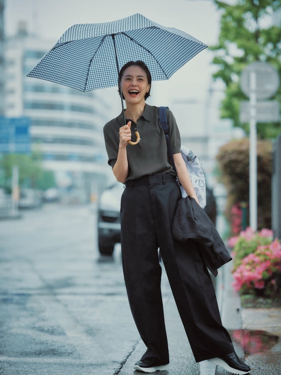 パンツ4万8400円、ポロニット3万800円（ともにハイク／ボウルズ） 手に持ったジャケット1万8700円（カランシエル／シップス インフォメーションセンター） バックパック2万3100円（アコック／ジャック・オブ・オール・トレーズ プレスルーム） 靴4万1800円（プレインピープル／プレインピープル青山） 傘1万5400円（トラディショナル ウェザーウェア／トラディショナル ウェザーウェア ルミネ有楽町店）