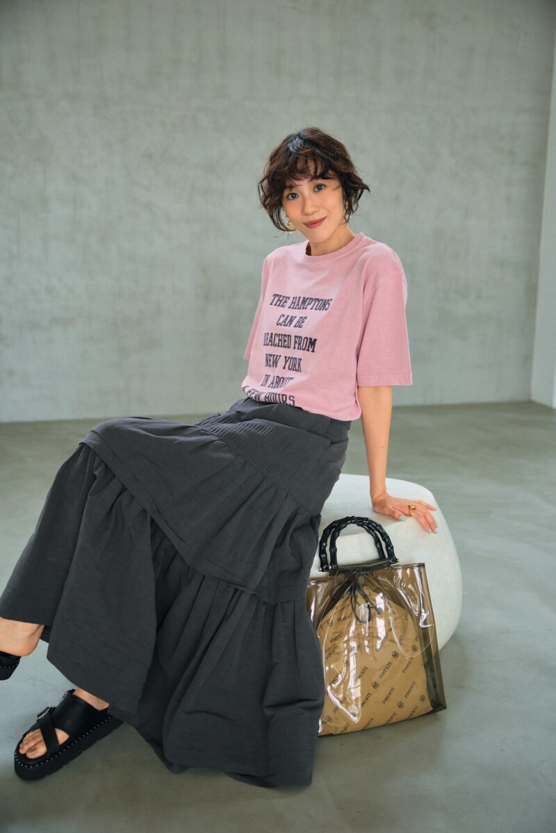 グレージュのティアードスカー トでシックに。Tシャツのタイポ グラフィーもグレージュのもの を選んで、さらにすっきりと洗練 された着こなしに。Tシャツ64 90円（デッサン／ワールド プレ スインフォメーション） スカー ト7万7000円（オブリオ） バッ グ1万6500円（ピモンテ） サン ダル1万8150円（ダイアナ／ダ イアナ 銀座本店） イヤリング 4950円（MU）、リング2530円 （シースキー／ともにロードス）