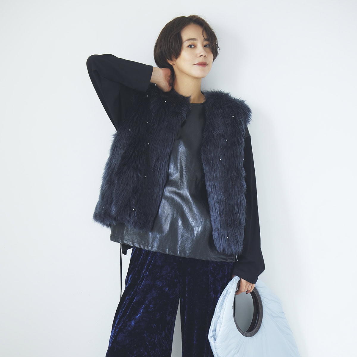 ネイビーのビジュー付きフェイクファーのベストとベロアパンツ、黒のフェイクレザー切り替えトップスでクールに。